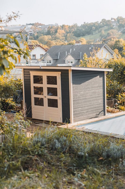 Modernes Gartenhaus in Anthrazit mit heller Doppeltür im Herbstgarten