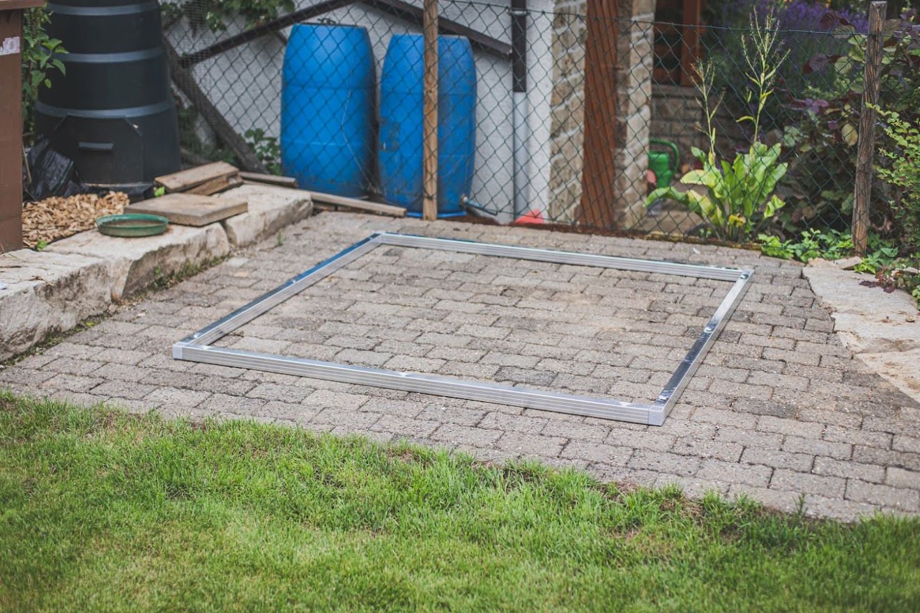 Biohort Bodenrahmen auf gepflasterten Fundament vor zwei blauen Regentonnen