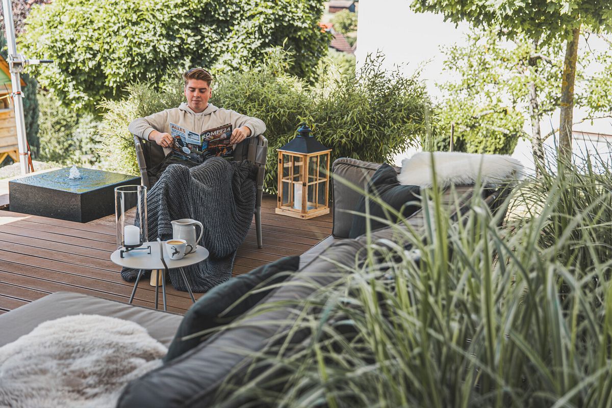 Person sitzt im gemütlichen Sessel der modernen Sitzgarnitur auf der Terrasse und ließt eine Zeitschrift