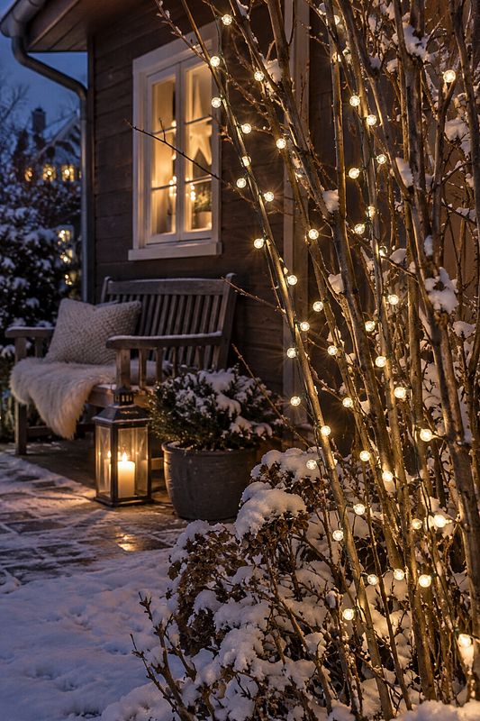 Lichterkette und Laternen schaffen mehrere Lichtpunkte auf einer winterlichen Terrasse