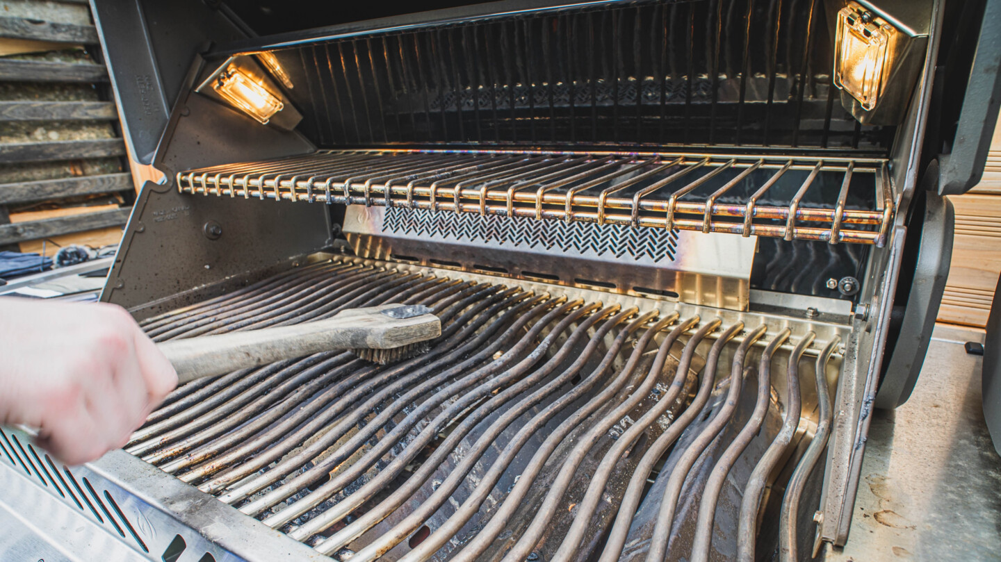 Ein schmutziger Grillrost in einem Gasgrill wird mit einer Grillbürste geputzt