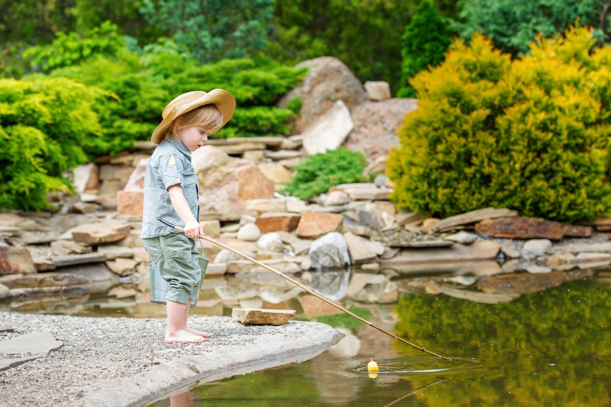 Junge am Teich Kleiner Junge mit Strohhut angelt im Teich.
