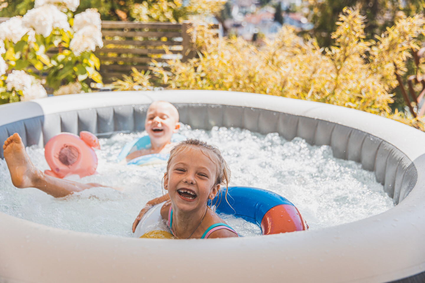 Zwei Kinder spielen ausgelassen mit aufblasbaren Gummitieren im Pool