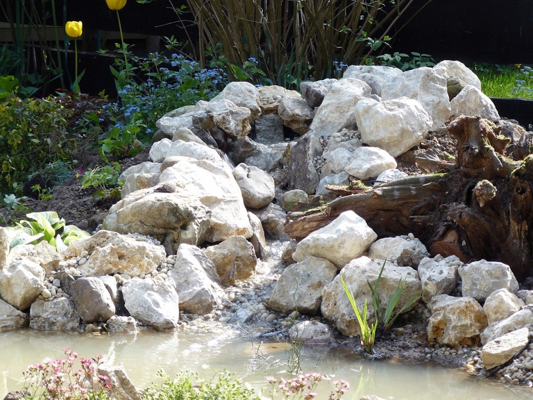 Teichbau Schritt 8: Der Bachlauf wird mit Steinen ausgekleidet. Der Bachlauf ist mit Steinen ausgekleidet, so dass keine Folie mehr zu erkennen ist.