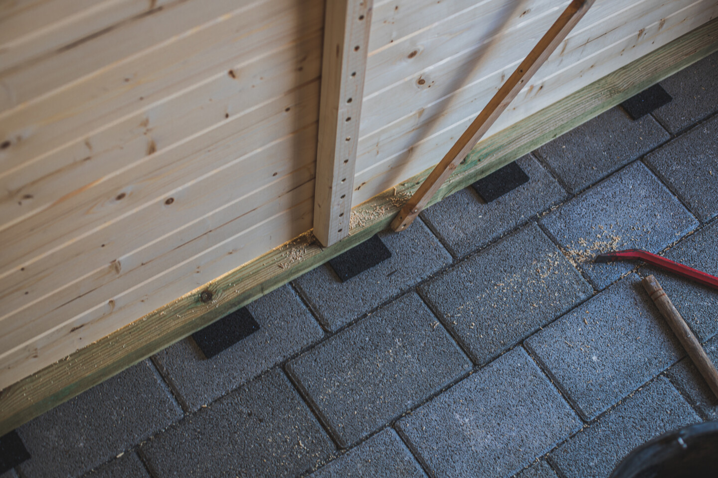 Nachdem das Gartenhaus an seine endgültige Position gesetzt wurde, werden Pads aus Gummigranulat untergelegt.