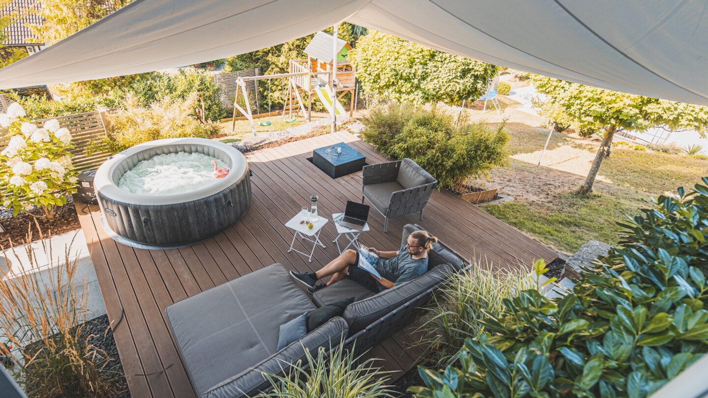 Whirlpool auf einer gemütlichen Terrasse Eine gemütlich eingerichtete Holzterrasse mit Möbeln und Whirlpool unter einem großen Sonnensegel
