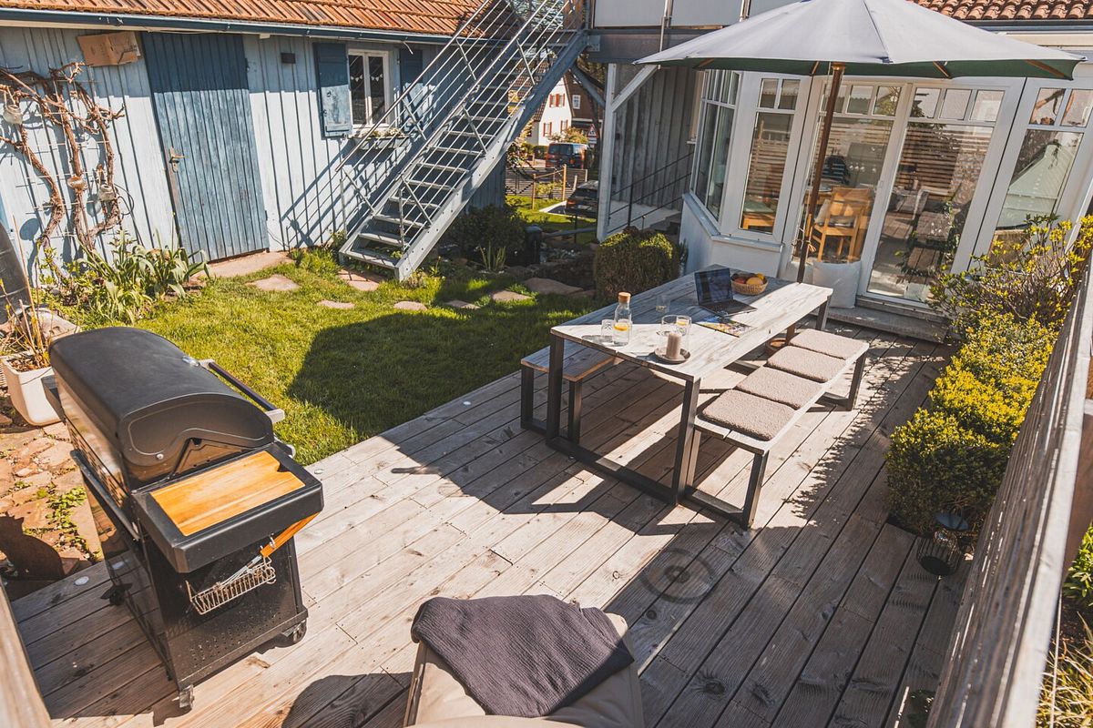 Holzterrasse im Hintergarten in Verlängerung zu einem Wintergarten mit Tischgarnitur und großem Grill