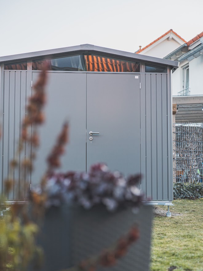 Biohort Panorama mit Doppeltür im Fokus hinter Blumenpflanzen im Reihenhausgarten vor Gabionenwand 