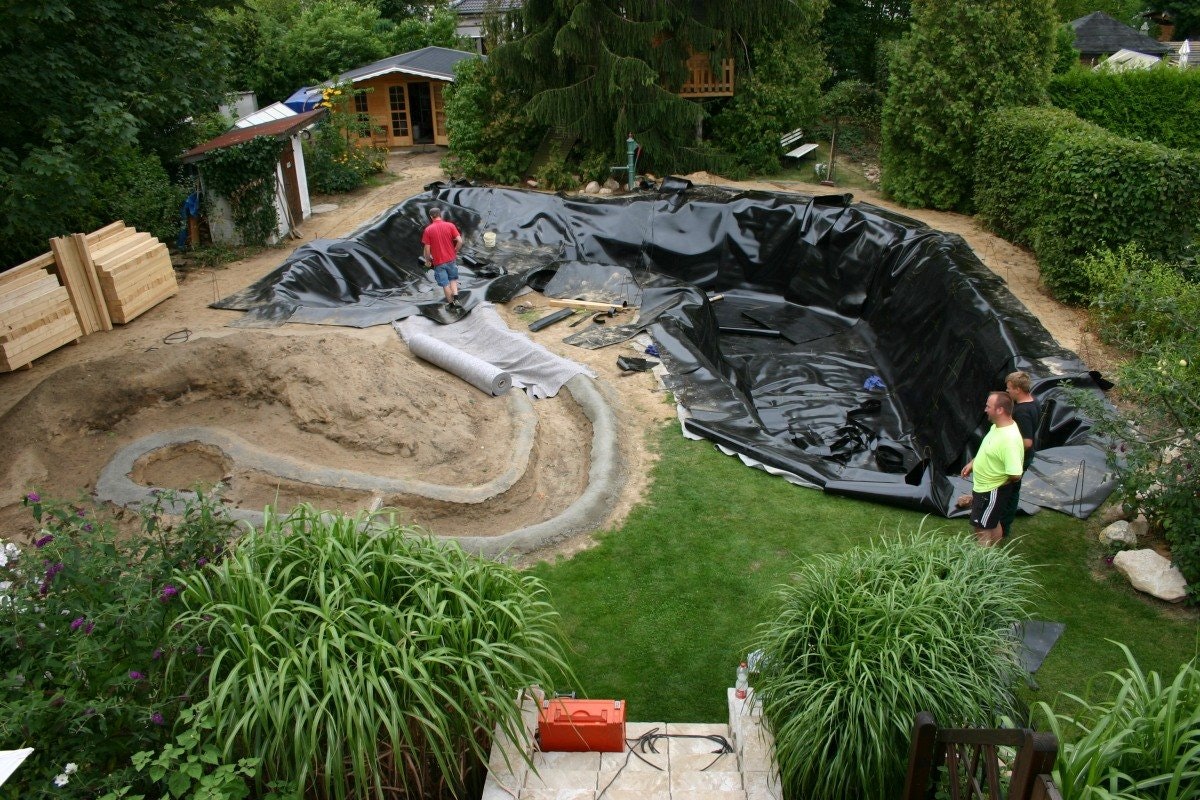 Auskleiden eines großen Schwimmteichs mit Teichfolie. Links im Bild wird der Zulauf noch mit Teichvlies ausgekleidet während rechts im Bild schon die Teichfolie verlegt ist.