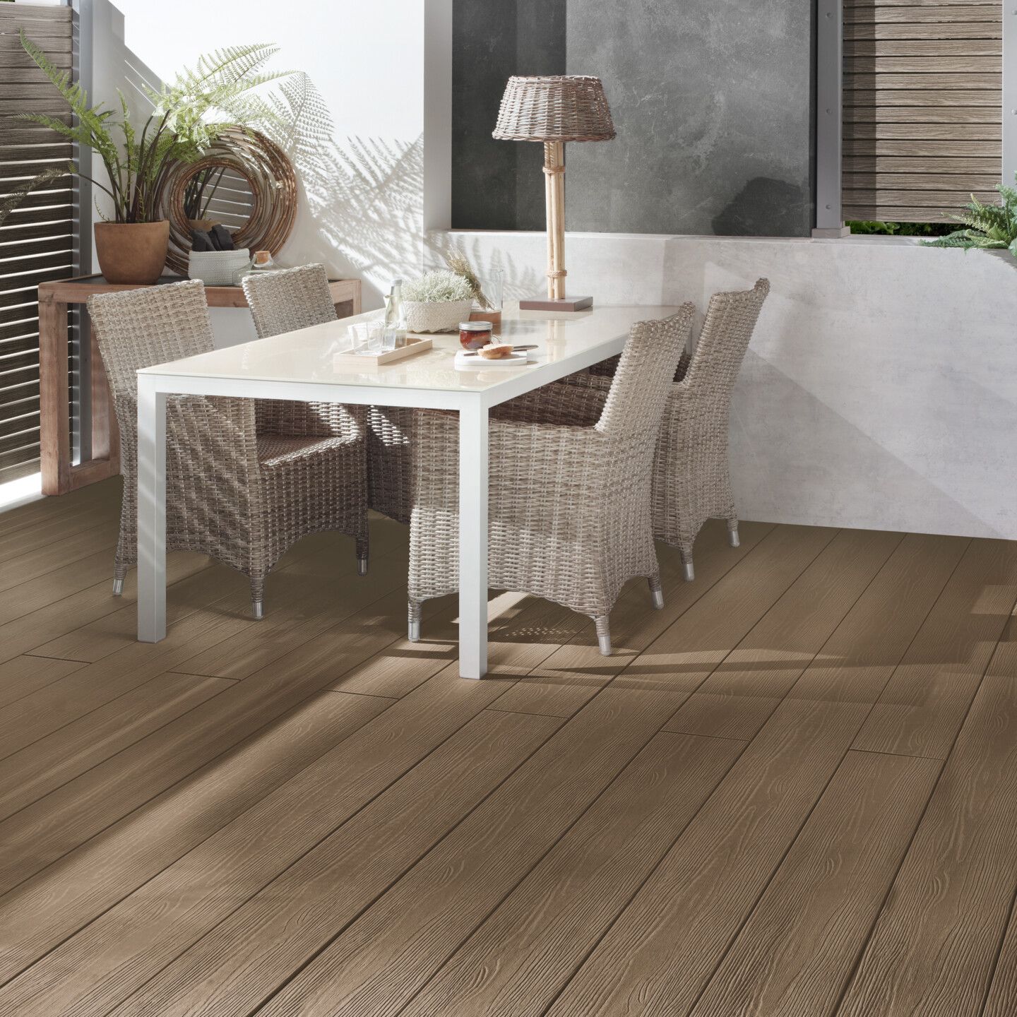 Terrasse aus graubraunen Dielen mit modernem weißen Tisch und Rattan Stühlen