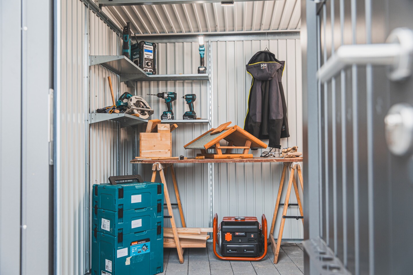 Verschiedene Werkzeuge der Marke Makita und Einhell wie Akku-Handkreissäge, Akku-Bohrschrauber, Akku-Schlagschrauber, MakPac, Akku-Baustellenradio, Akku- Arbeitsleuchte und Stromerzeuger und Arbeitskleider der Marke Helly Hansen wie Softshelljacke im inneren des Biohort Avantgart