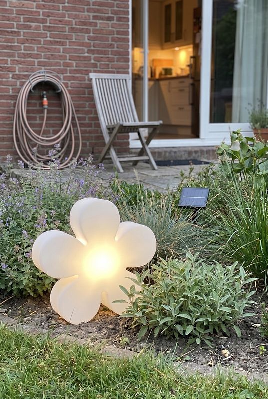 Eine blumenförmige LED Gartenlampe steht in einem Kräuterbeet