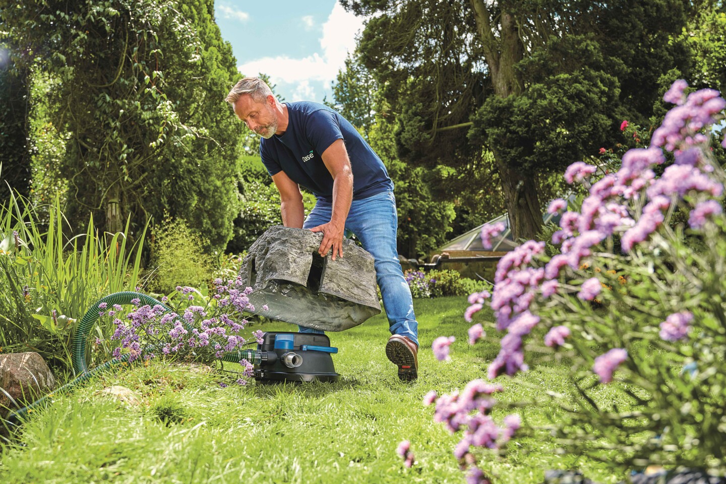 Ein Mann versteckt einen Teichfilter unter einem Stein