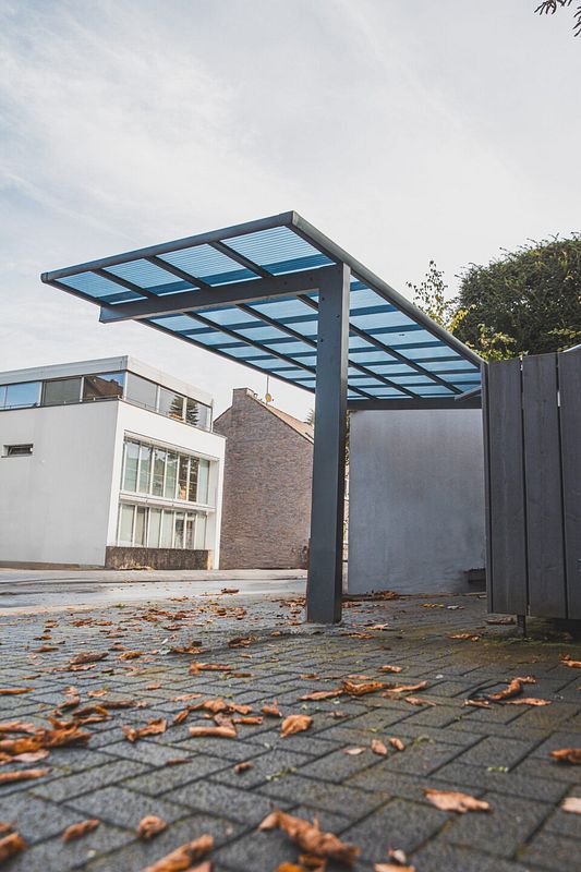 Graues Metallcarport mit transparentem Dach vor Häusern