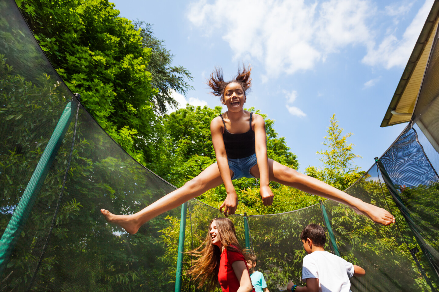 4 Kinder springen auf einem Gartentrampolin auf und ab