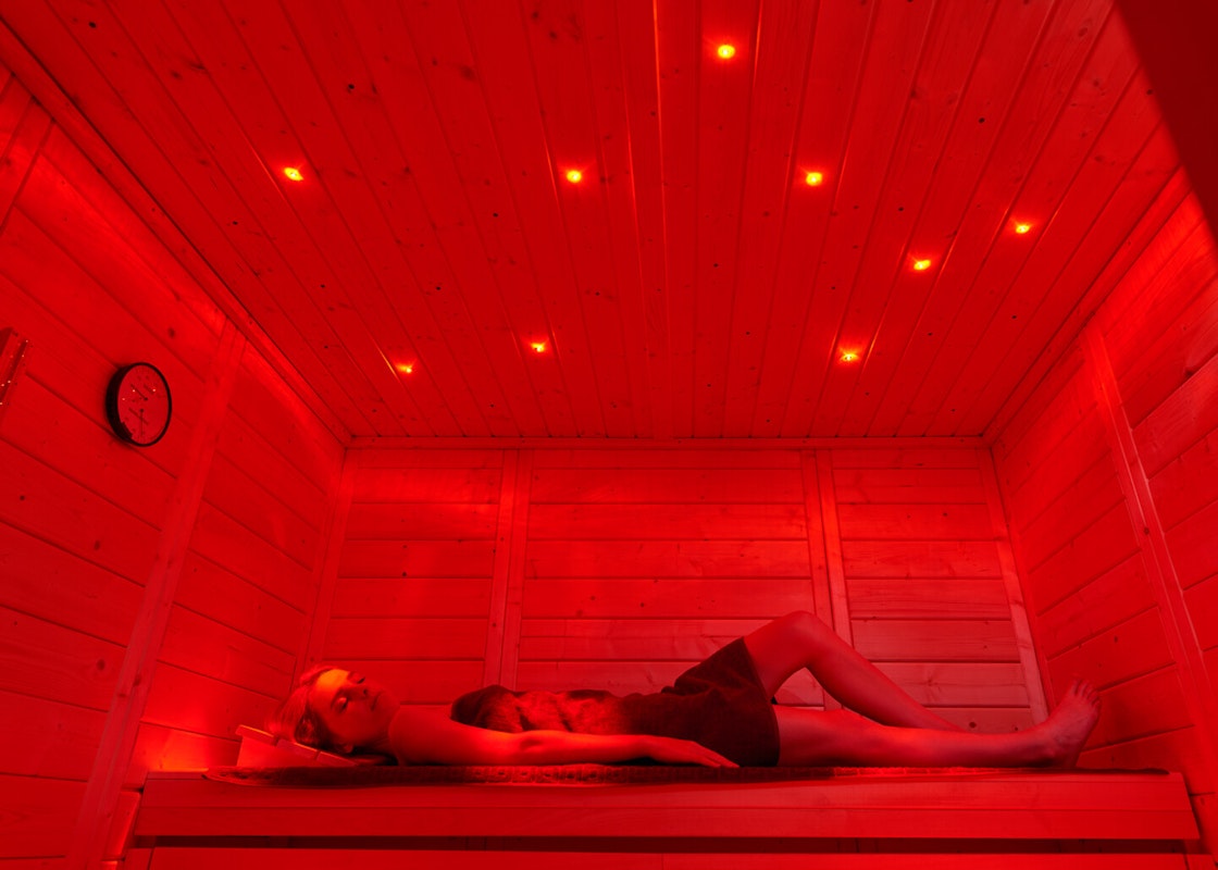 Sauna mit Farblicht und Sternenhimmel Eine Frau entspannt auf einer Saunabank mit rotem Licht und Sternenbeleuchtung