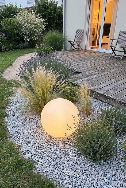 Eine große kugelfärmige LED Outdoorleuchte zwischen Ziergräßern an einer Terrasse