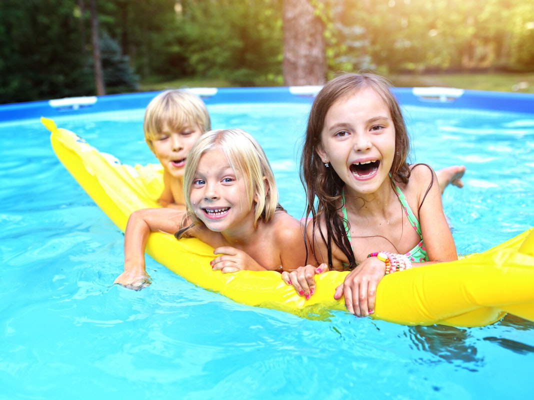 Wasserspaß für alle 3 Kinder auf einer Luftmatratze im Pool