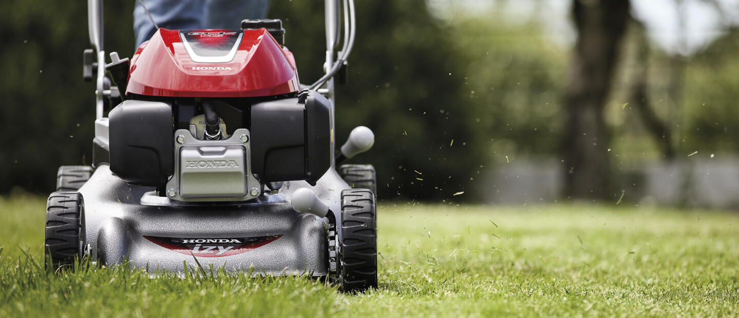 Person mäht Rasen mit einem roten Rasenmäher von Honda