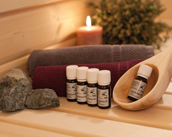 Ätherische Öle Ätherische Öle für die Sauna mit einer hölzernen Schöpfkelle und Handtüchern, sowie einer Kerze im Hintergrund