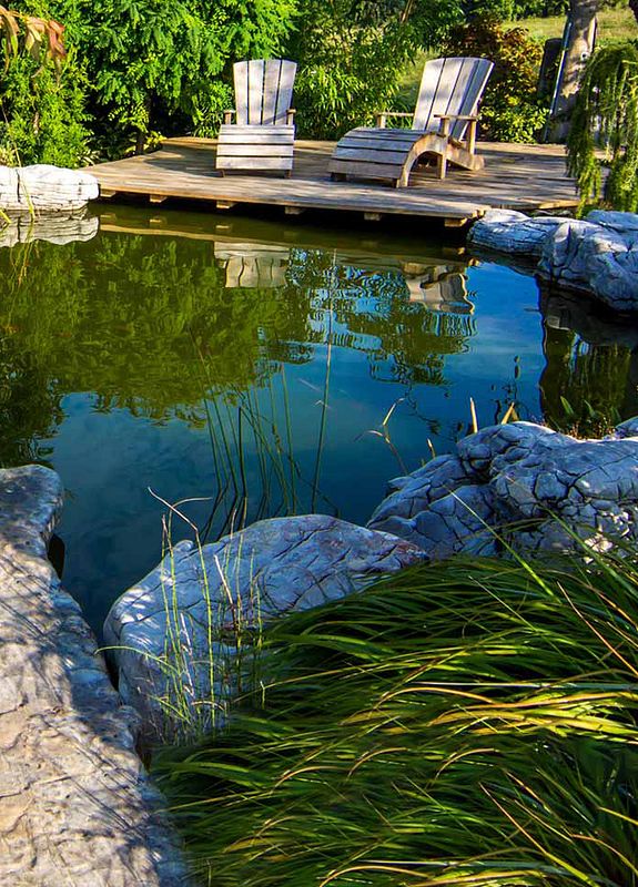 Ein idyllischer Gartenteich mit angrenzender Holzterrasse und zwei Liegestühlen