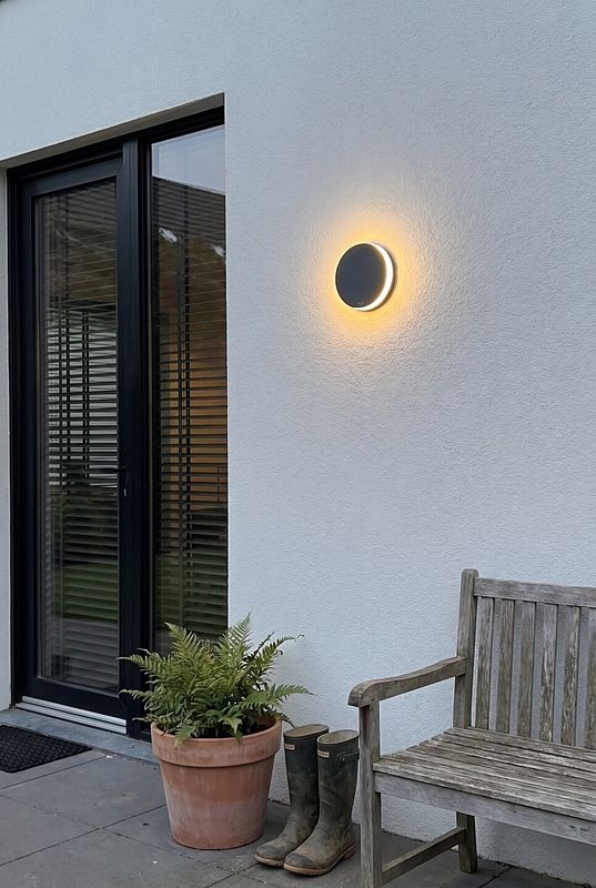 Eine Wandleuchte mit rundem Lichtsrahl zwischen Balkontür und Sitzbank aus Holz