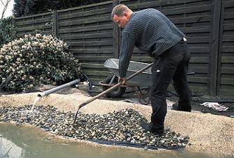 Schritt 9: Gestaltung des Randbereichs mit Steinen Teichbau Schritt 9: Der Ranbereich wird mit Kieselsteinen gefüllt und mir einer Schaufel verteilt.