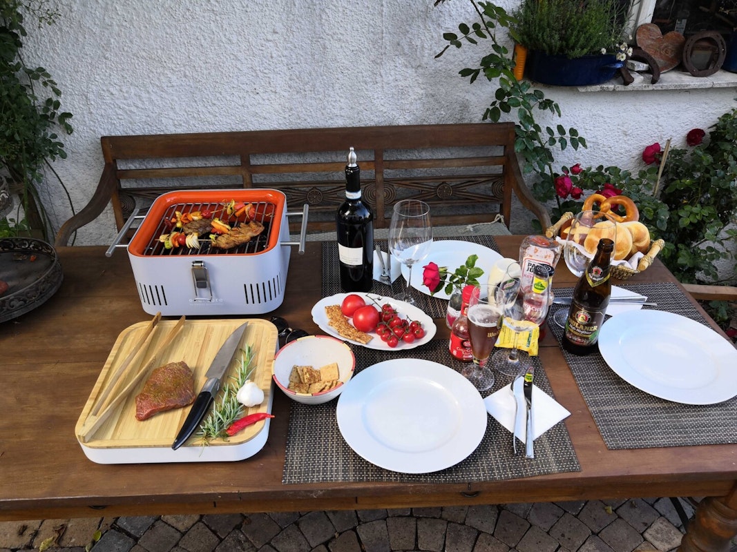 Der Grillrost bietet ausreichend Platz um drei Personen zu begrillen. Voller Grillrost, Gedeckter Tisch, Schneidebrett mit Grillzange, Messer, Stück Rinderfilet, Rosmarin, Knoblauch und Chili