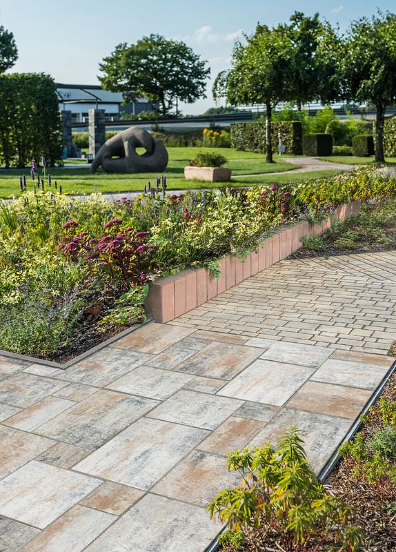 Terrassenplatten aus Beton führen über einen weg in einen parkählichen Garten