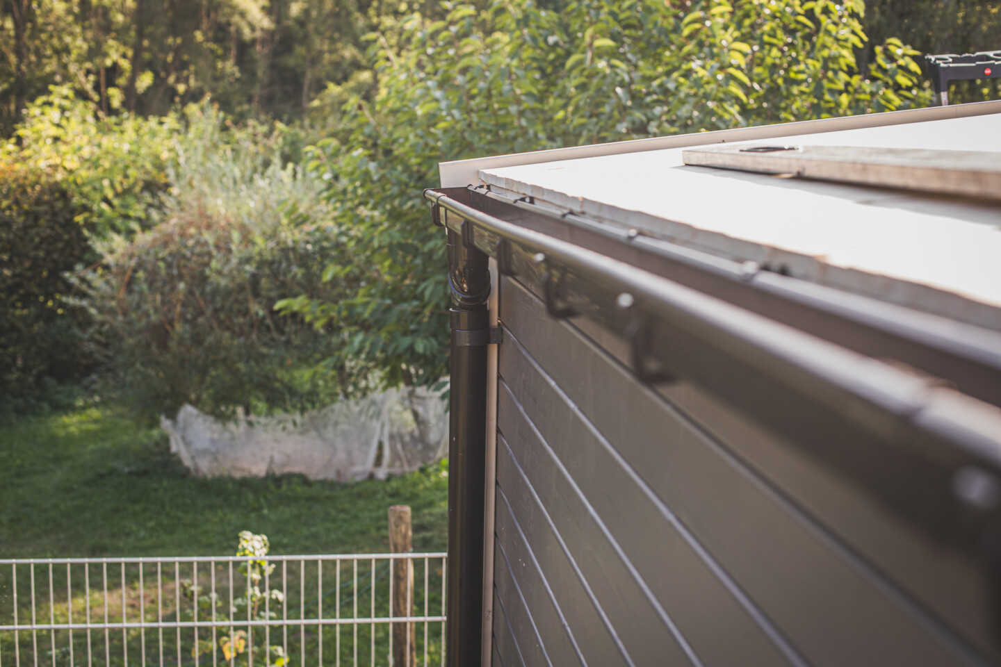 Die Dachrinne hat ein leichtes Gefälle nach einer Seite, an der ein Fallrohr angebracht ist.