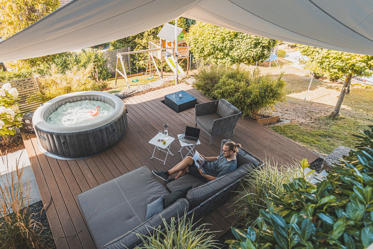 Große Terrasse mit Loungegarnitur Wirlpool und Wasserspiel in einem Familiengarten mit Kinderspielhaus