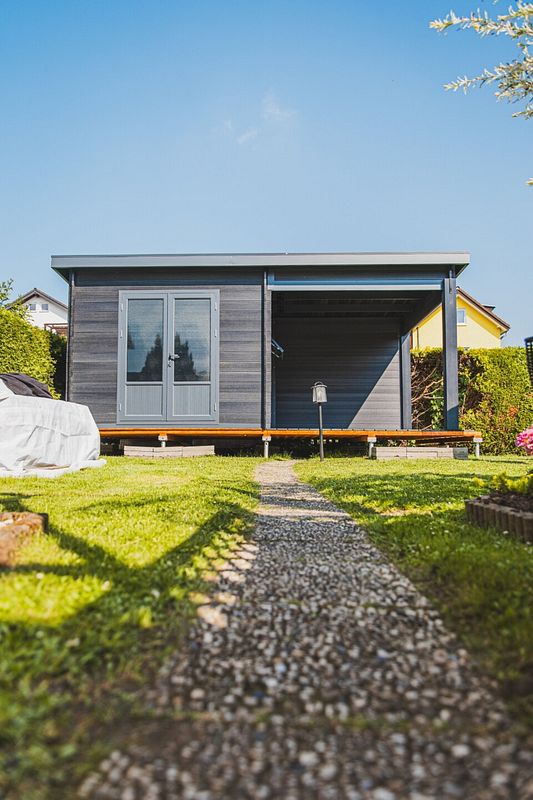 Graues Gartenhaus mit Anbau und Terrasse im gepflegten Garten