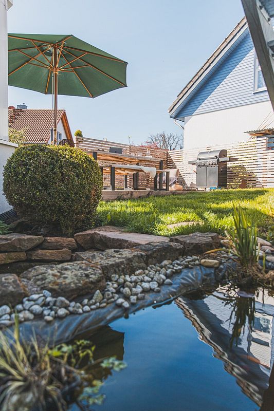 Kleiner Folienteich im modernen Garten neben Grillecke