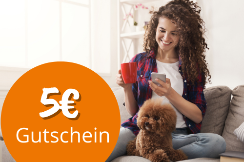 Frau sitz auf der Couch und schaut in ein Smarphone. Ein kleiner Pudel sitzt vor ihr