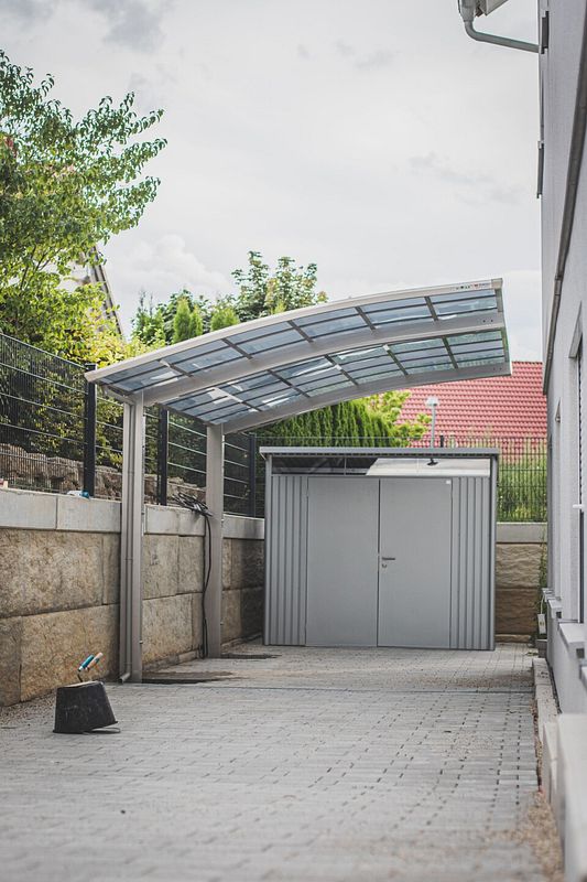 Ein gepflasterter Hof mit abgerundetem Carport neben einem Haus