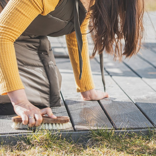 Frau kniet auf der Terrasse um diese mit einer Bürste zu reinigen