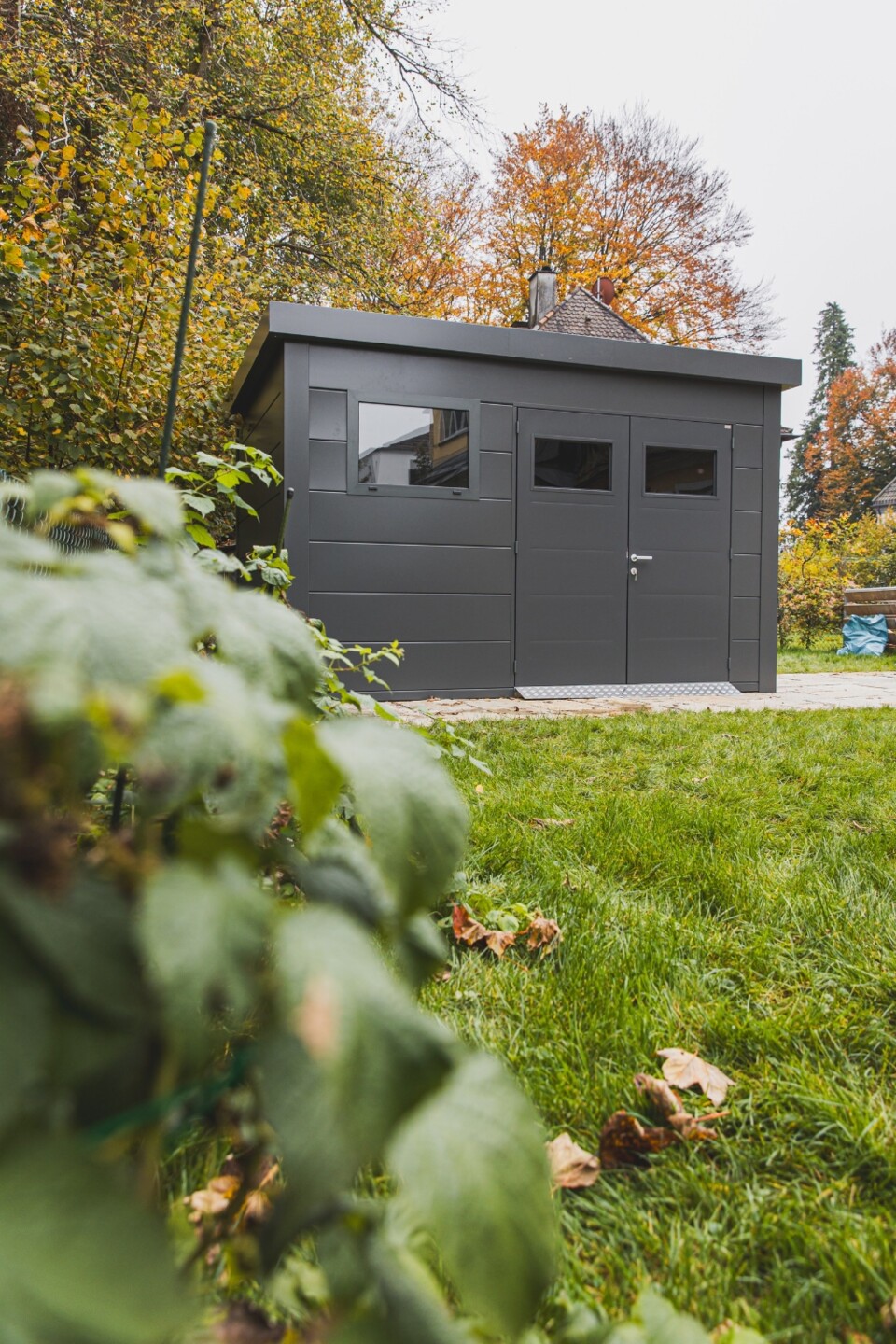 Anthrazitfarbenes Gerätehaus mit Flachdach im herbstlichen Garten