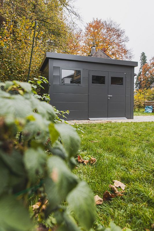 Anthrazitfarbenes Gerätehaus mit Flachdach im herbstlichen Garten