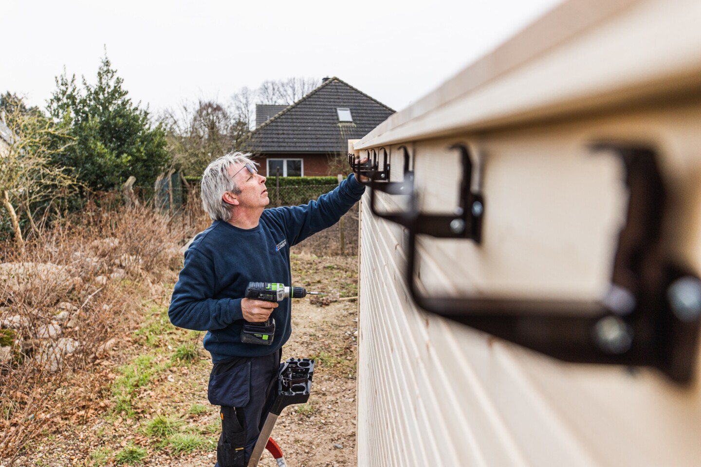 Die Aufhängungen für die Dachrinne werden auf der Rückseite des Gartenhauses angeschraubt