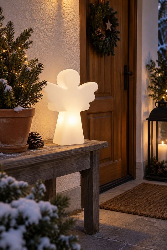 Ein LED Engel auf einer Holzbank neben einer Haustüre