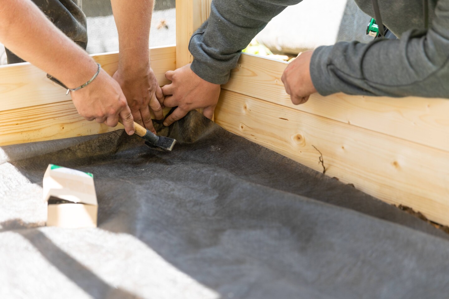 Das Bodenschutzvlies für einen Sandkasten wird befestigt