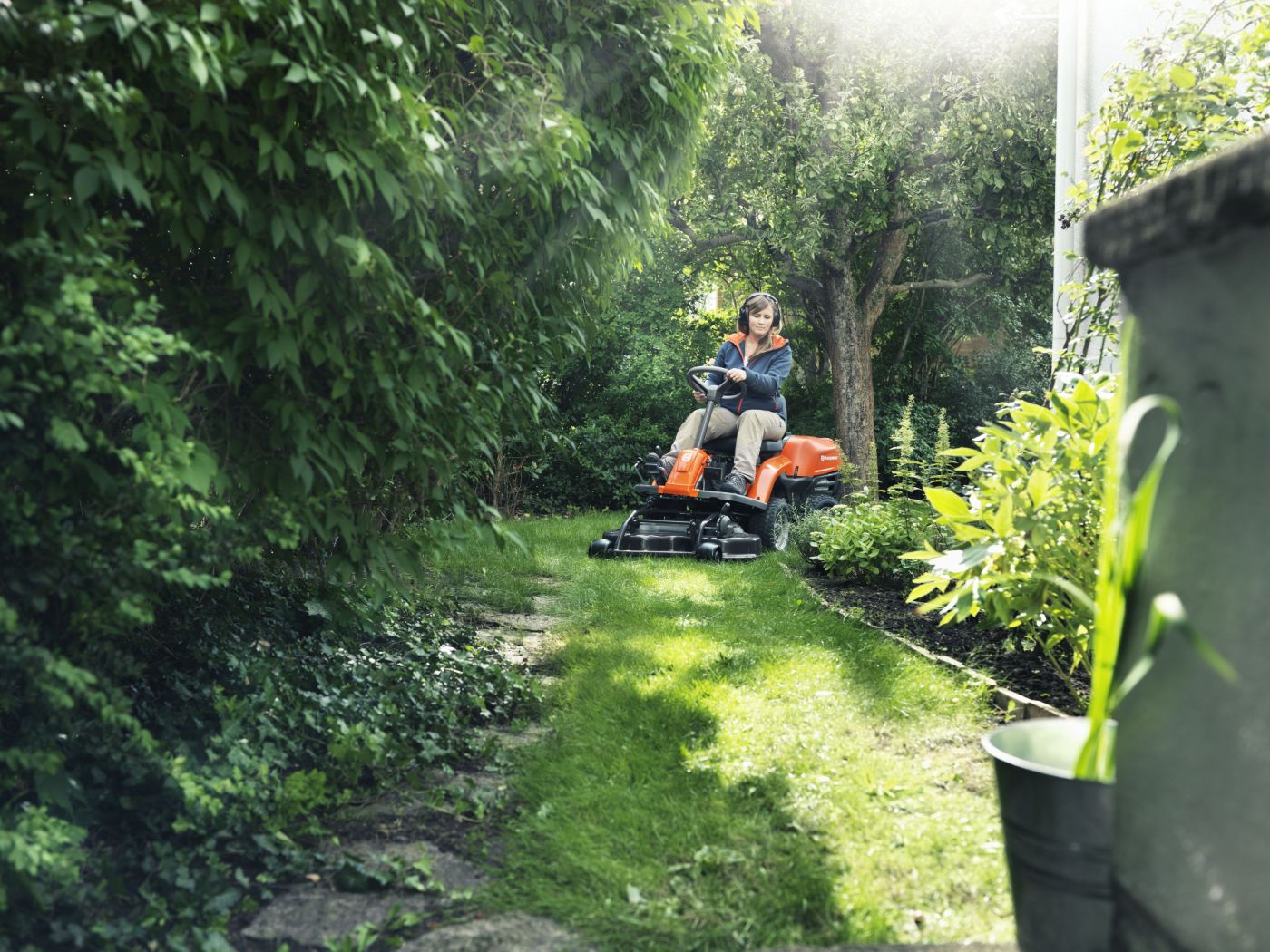 Frau fährt mit einem Aufsitzrasenmäher hinter einem Haus