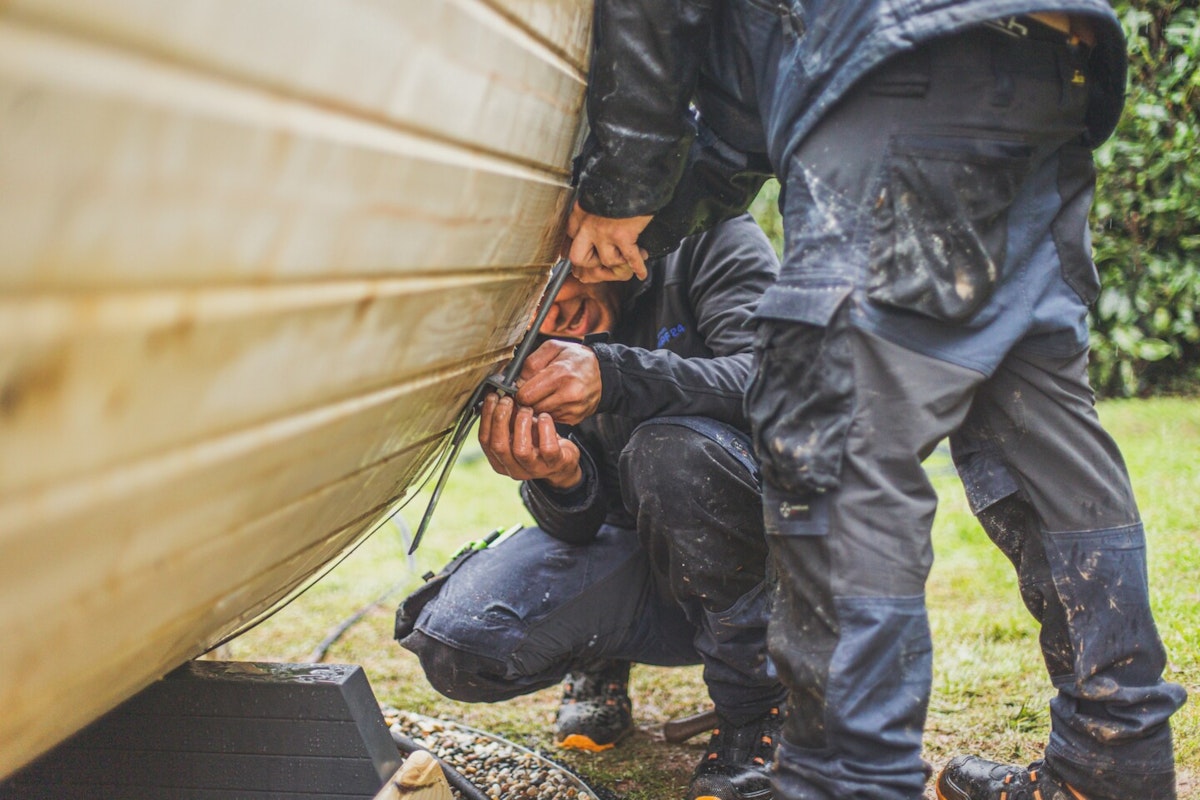 Festziehen des Metallbandes Das Band aus Metall wird festgezogen und hält die Blockbohlen zusammen